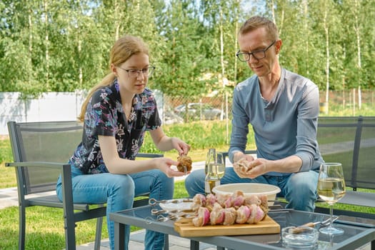 Father and daughter skewering meat and mushroom while sitting in the backyard