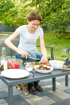 Middle-aged woman preparing salad outdoors while sitting in backyard