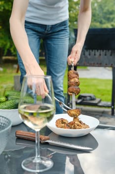 Unrecognizable woman removes grilled champignons from a skewer with a fork