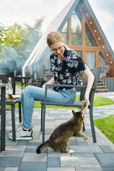 Girl plays with a cat while relaxing on the lawn of a country house during a picnic