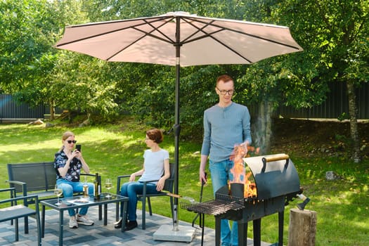 The daughter takes a photo of her father putting a birch log on the grill