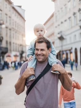Portrait of smiling father carrying his toddler child piggyback around city on family vacations. Happy father's day