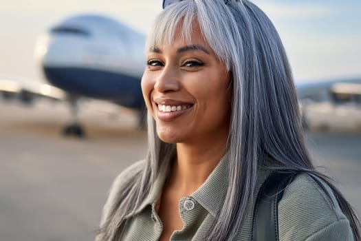 Mature smiling grey-haired woman at airport with airplane in the background.