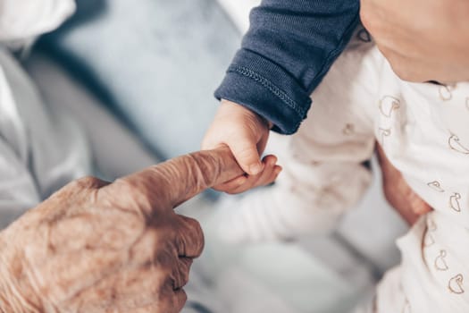 Circle of life. Little baby boy child hand holding great grandmother wrinkled finger. Intergenerational help and solidarity concept.