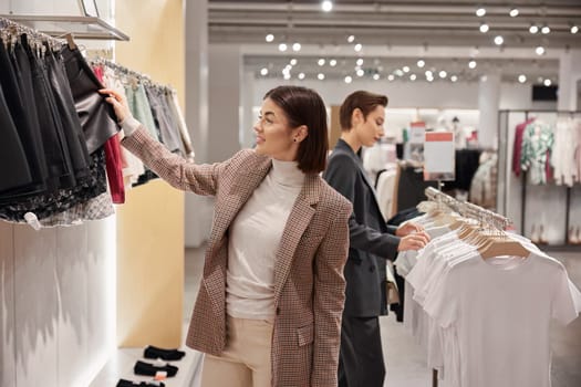 Two elegant woman enjoying shopping at fashion clothes boutique. Adult female friends searching trendy outfit together. Sale and consumerism concept