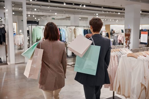 Positive emotions and relaxed expression during purchase time on weekends. Two woman shoppers with shopping bags view from back