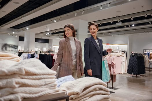 Cute girls are choosing casual knitted sweaters smiling while doing shopping at fashion boutique