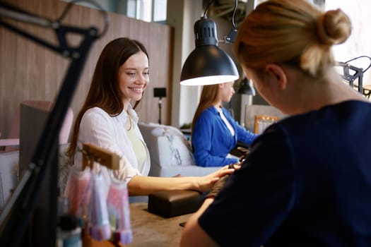 Happy laughing young woman friends getting manicure and gossiping together. Professional nail salon and satisfied clients