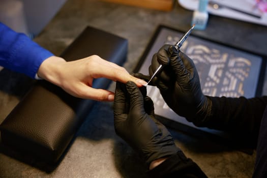 Closeup of master manicurist doing manicure for female client at beauty salon. Beautician correcting cuticle cleaning nails with sterile tool
