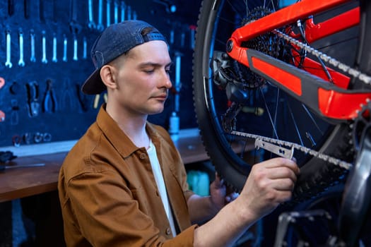 Young repairman providing bike chain stretch measurement with special checker tool at workshop. Bicycle repair service