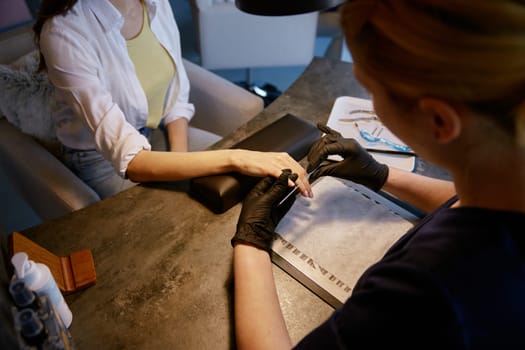 Woman client enjoying manicure at beauty salon. Professional manicurist working with customer providing procedures for nails