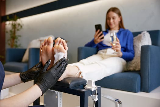 Barefoot client at pedicure procedure in luxury beauty spa salon. Female podiatrist cleaning feet with napkin before toenail and skin care therapy