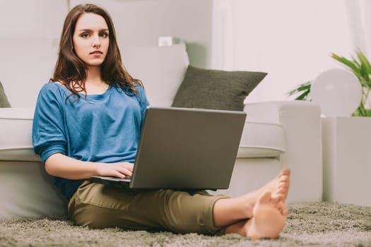 woman, dressed casually in a blue shirt, sits with her laptop, reflecting on future uncertainties. Her pensive gaze suggests a deep inner dialogue about work-life balance and societal expectations