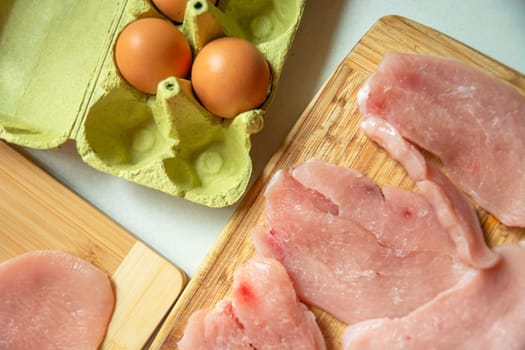 Eggs in a carton box and meat for chops on the table, top view
