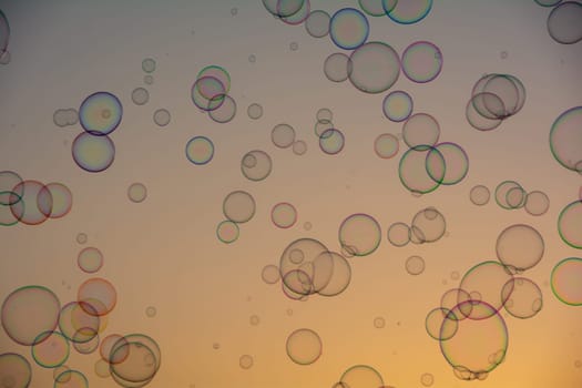 Many colorful soap bubbles float in the orange sky at sunset