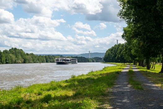 A pleasure boat sails along a river, with green nature, blue sky and white clouds