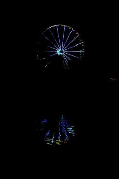 Ferris wheel with colorful lighting at dark night and reflections in the water