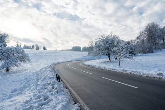 Snow landscape with trees, road and blue sky with clouds