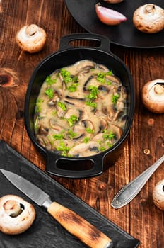 Brown champignon mushrooms stewed in sour cream on wooden background