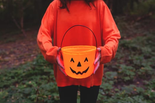Girl in an orange sweater holding a pumpkin bucket, perfect for autumn and Halloween themes. The image captures the festive spirit with a focus on seasonal celebration and decoration