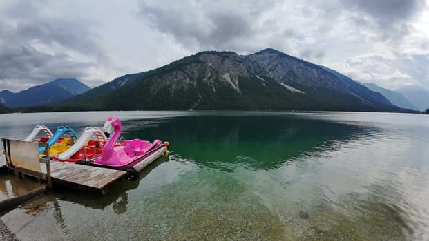 Colorful pedal boats on the Plansee in Austria with a dark cloudy atmosphere