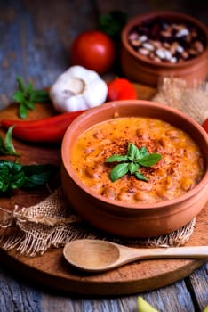 Traditional baked beans in tomato sauce cooked in retro clay pot with spices and vegetables. Homemade healthy cuisine.