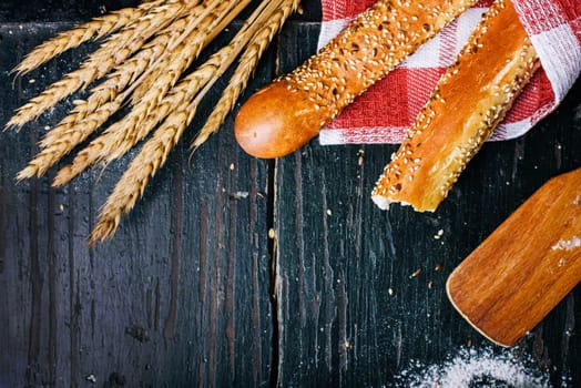 Fresh french baguette bread, organic flour and wholegrain wheat on dark vintage wooden board form above. Top view of traditional baked bread. Bakery shop menu background.