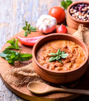 Traditional baked beans in tomato sauce cooked in retro clay pot with spices and vegetables. Homemade healthy cuisine.