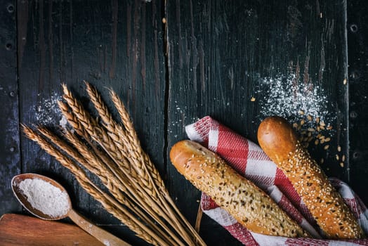 Fresh french baguette bread, organic flour and wholegrain wheat on dark vintage wooden board form above. Top view of traditional baked bread. Bakery shop menu background.