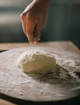 Man kneading and baking homemade pizza dough in the kitchen. Closeup on baker's hands preparing loaf of bread. Cooking and food preparation at home.
