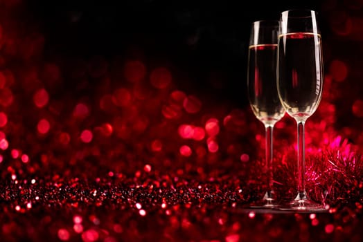 Two champagne glasses on sparkling red bokeh background. Celebration toast flutes. Valentine's day dinner invitation. Christmas and new year holiday party.