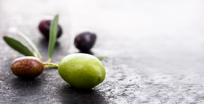 Closeup of fresh olive fruit on dark textured background with copyspace. Black and green organic olives with leaf. Spanish cuisine.
