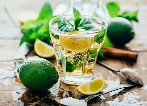 Fresh miojito cocktail with cuban rum, lime slices and mint herb on vintage wooden table. Summer beverage mohito hommade recipe with exotic fruit and cold liquor. Alcohol drink ingredients.