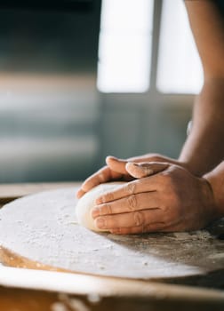 Man kneading and baking homemade pizza dough in the kitchen. Closeup on baker's hands preparing loaf of bread. Cooking and food preparation at home.