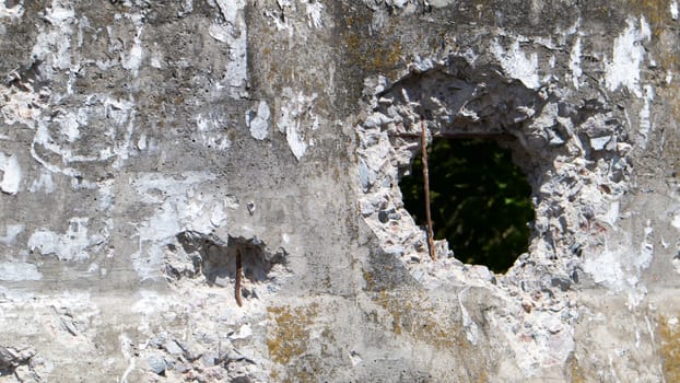 Photo of a broken cement wall or fence. Stone grunge odd wall with a hole. Damaged grungy crack and broken concrete wall