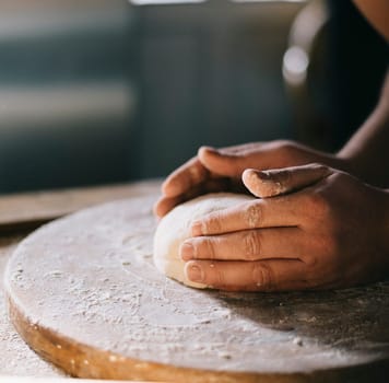 Man kneading and baking homemade pizza dough in the kitchen. Closeup on baker's hands preparing loaf of bread. Cooking and food preparation at home.