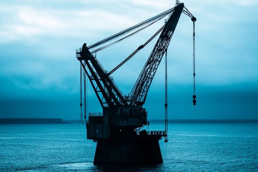 Silhouette of an offshore crane against a tranquil blue sea and sky at dusk, creating a serene industrial scene