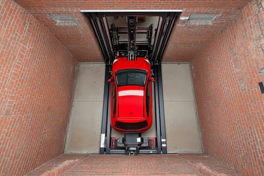Aerial view of a bright red car on an automated parking lift inside a brick-walled garage