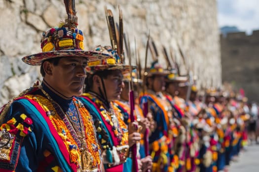 Line of men in ornate traditional Andean costumes with colorful hats and feathers performing at cultural festival.