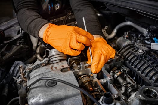 Experience the precision of a skilled mechanic's hands, clad in orange gloves, as they meticulously work to repair an open car engine in an auto service center, ensuring top-notch maintenance