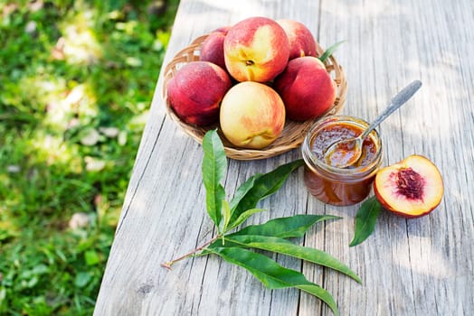 Peach jam or marmalade in a glass jar with ripe peaches, outdoors on sunny day