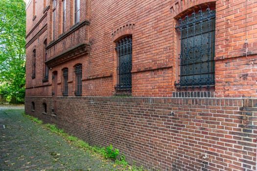 Perspective view of a brick exterior wall with barred windows with green trees in the background.
