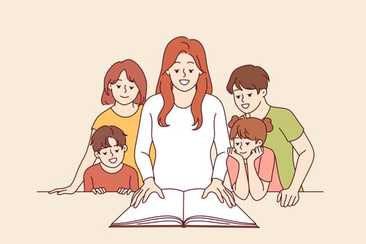 Woman teacher shows interesting book to happy children and smiles, rejoicing, giving kids knowledge. Children book for primary education and development of curiosity among elementary school students