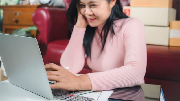 Businesswomen working business SME online at home her checking order from laptop for customer and online delivery for ready packing, Checking orders from customers with digital laptop, Small business.