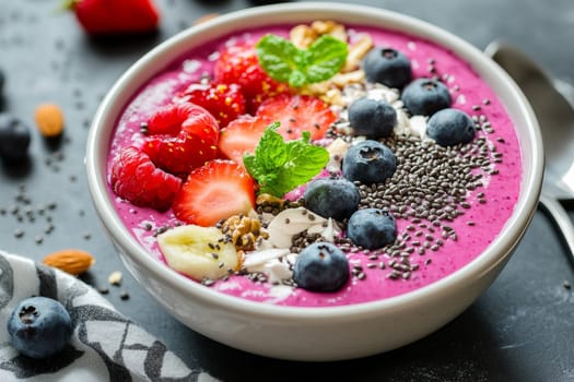 Pink smoothie bowl topped with strawberries, blueberries, and chia seeds.