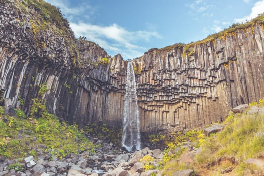 Svartifoss Waterfall in Iceland under a blue summer sky with clouds