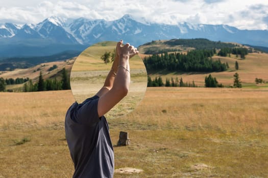 Man standing in in summer Altai mountains in Kurai steppe and holding circle mirror. Creative travel concept
