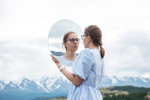 Woman standing in in summer Altai mountains in Kurai steppe and holding circle mirror. Creative travel concept