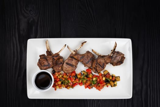 Roasted lamb ribs with vegetables on white plate on black wooden background