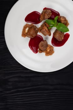 Delicacy Fried pork meat with zucchini puree and berries sauce decorated with mint on white plate on black wooden background